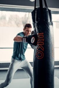 An adult male boxer in a gym actively punching a heavy bag for fitness training.