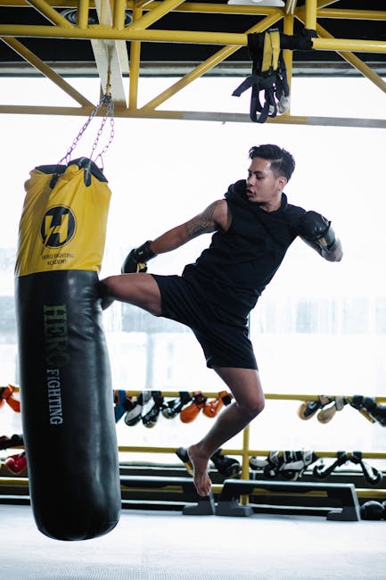 A man executing a powerful midair kick at a punching bag in a gym.